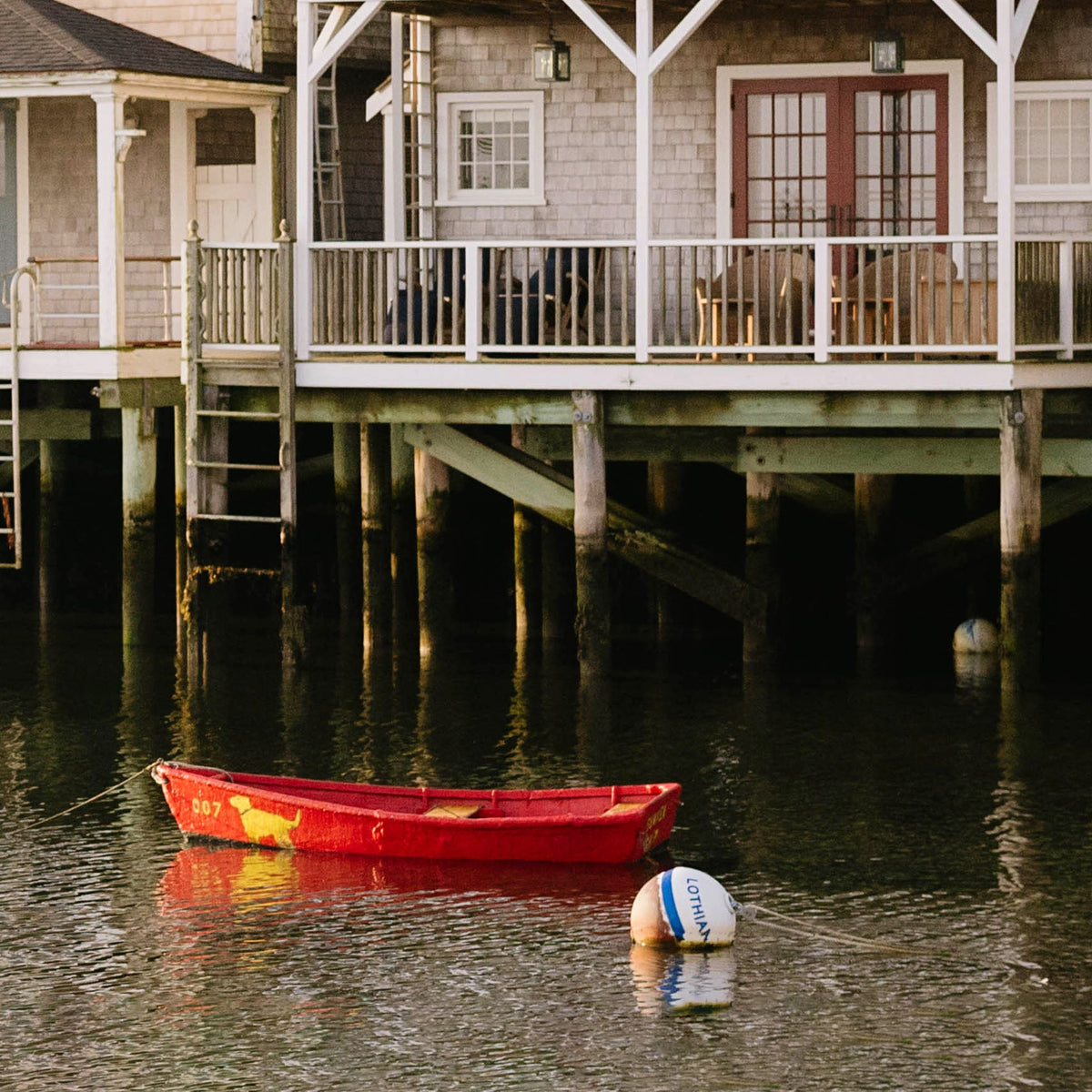 Close up of red rowboat on water near a wooden dock and house