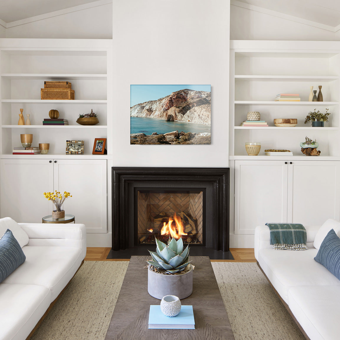 Modern living room with white walls, a fireplace, and a glass print of an Aegean shore above the mantel