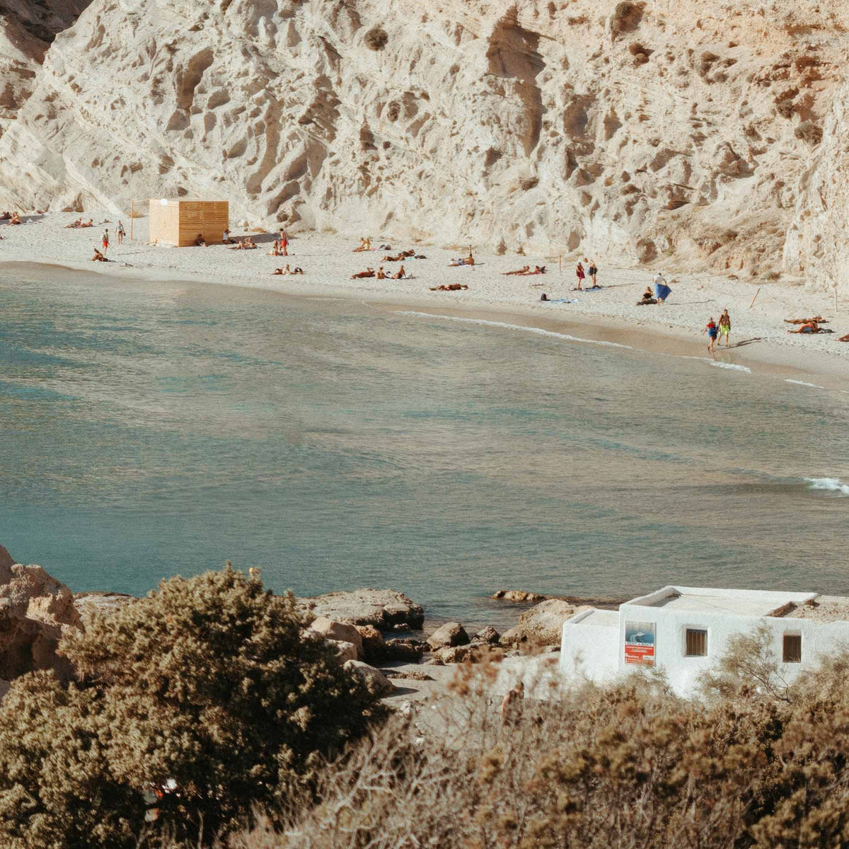 Close-up of beach scene with people, a building, and a cliff in the background.