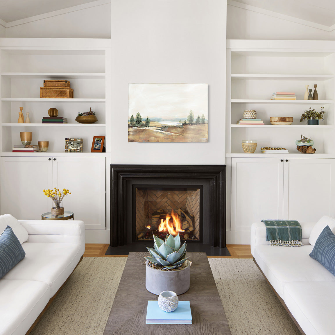 Living room with white walls, a fireplace, and a glass print of a painted landscape above the mantel. 