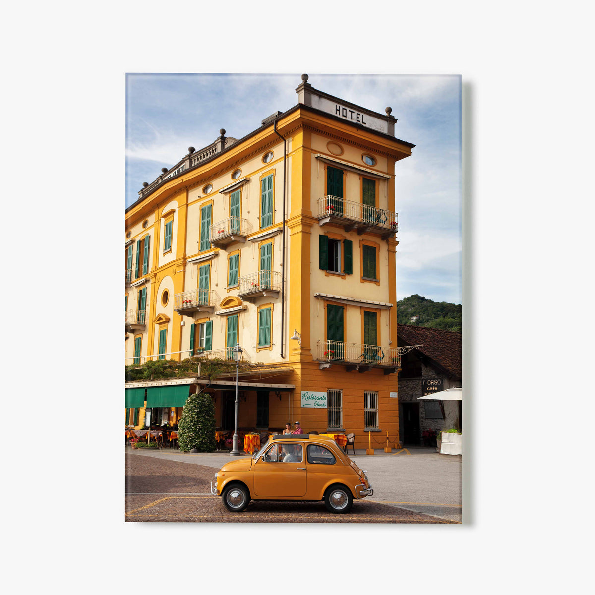Yellow vintage car parked in front of a yellow hotel with green shutters.