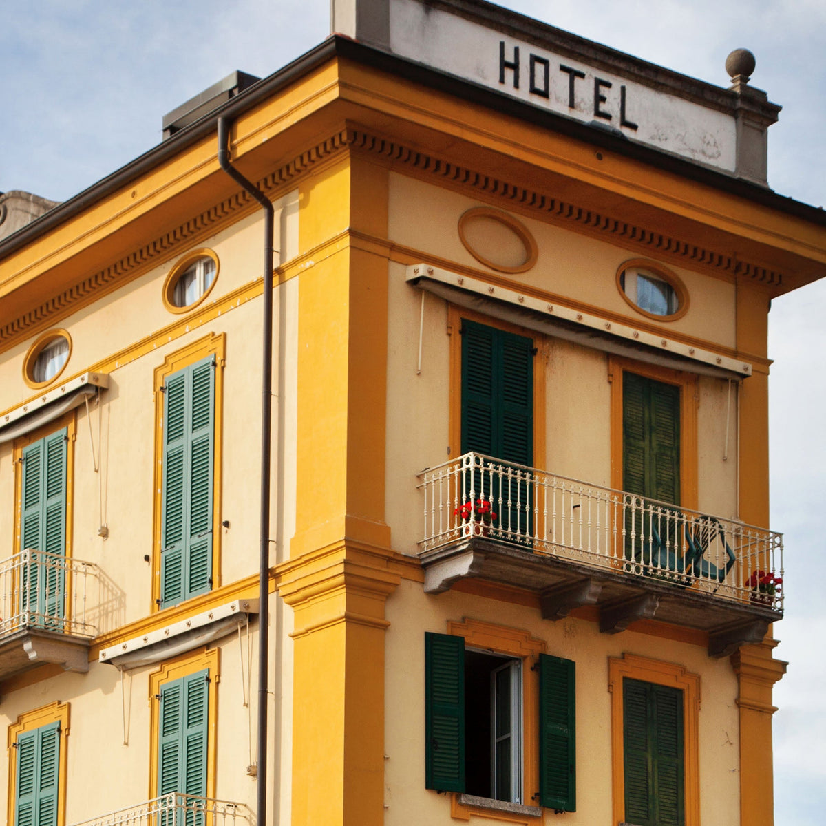 Close-up of yellow hotel building with green shutters and a balcony.