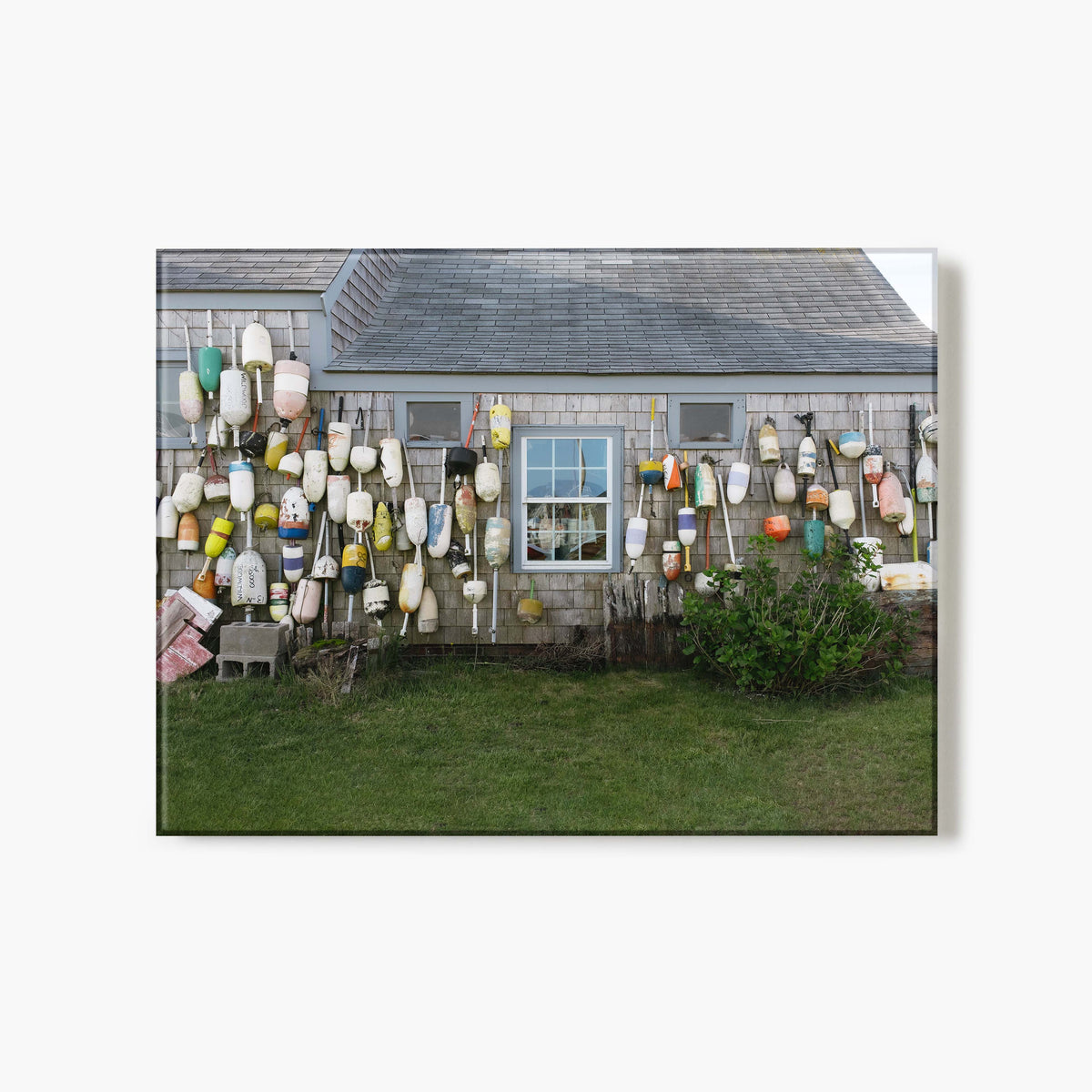 Glass print of a house exterior with a wall of colorful buoys and fishing equipment.