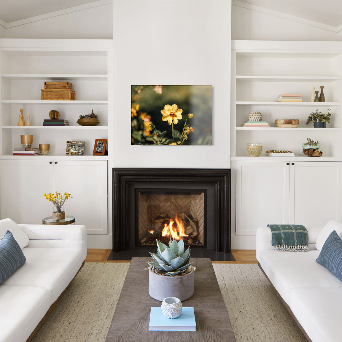 Modern living room with white walls, a fireplace, and a glass print of a yellow flower with a bee in the center.