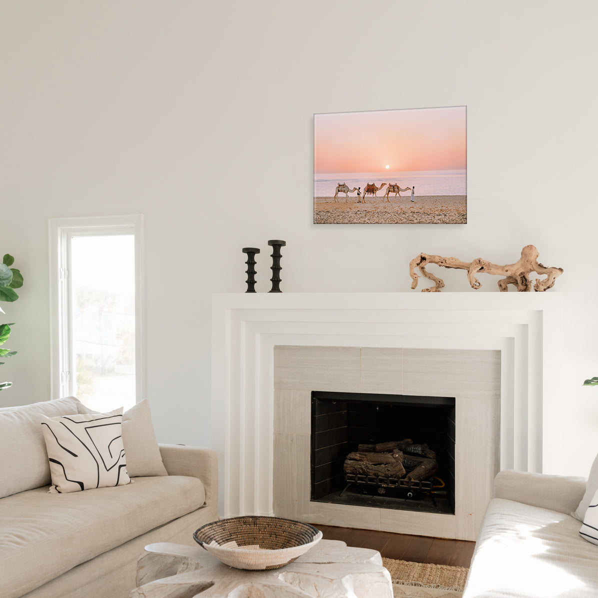 Living room with a fireplace, couch, and a glass print of camels being led on a beach at sunset.