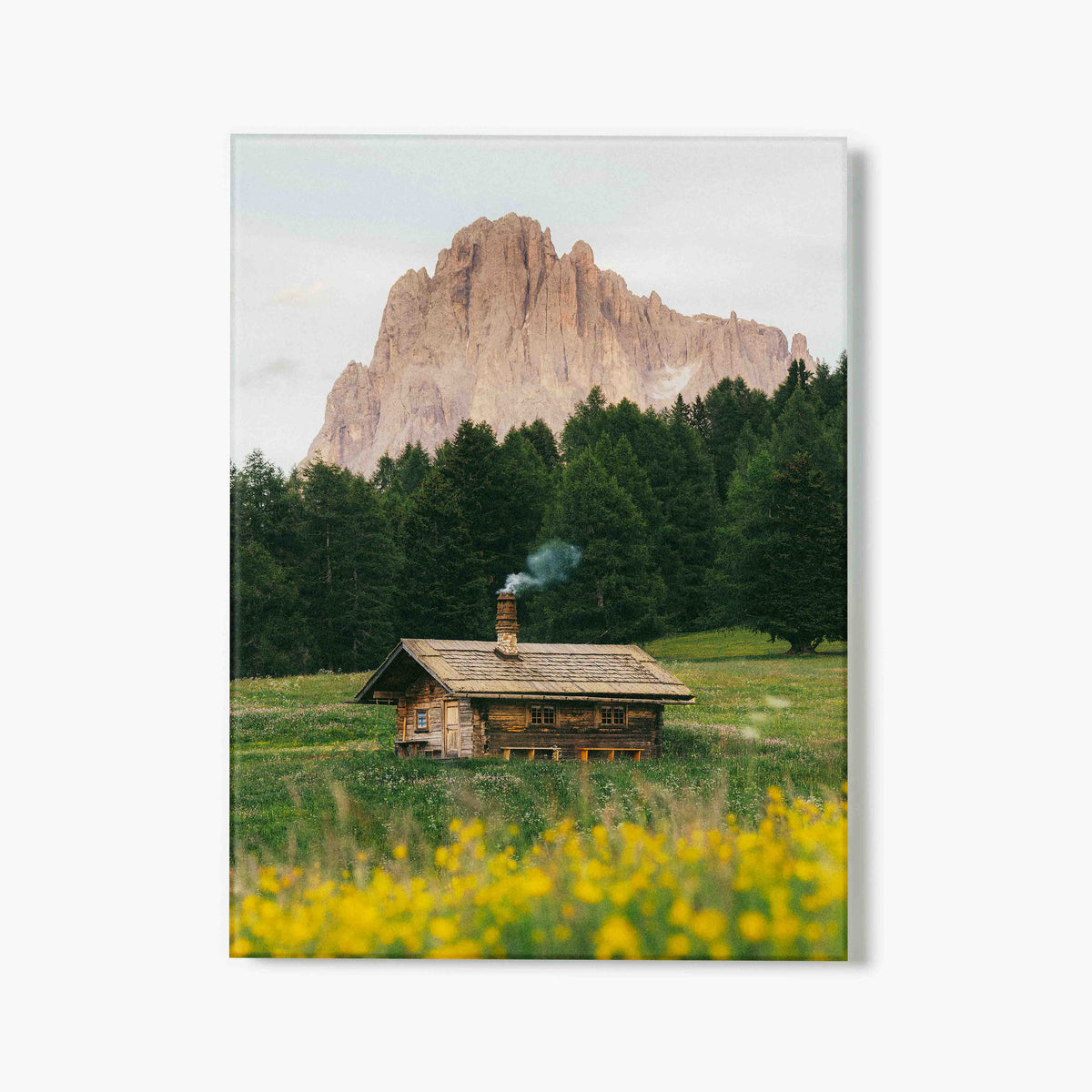 Glass print of wooden cabin in a field with mountains in the background