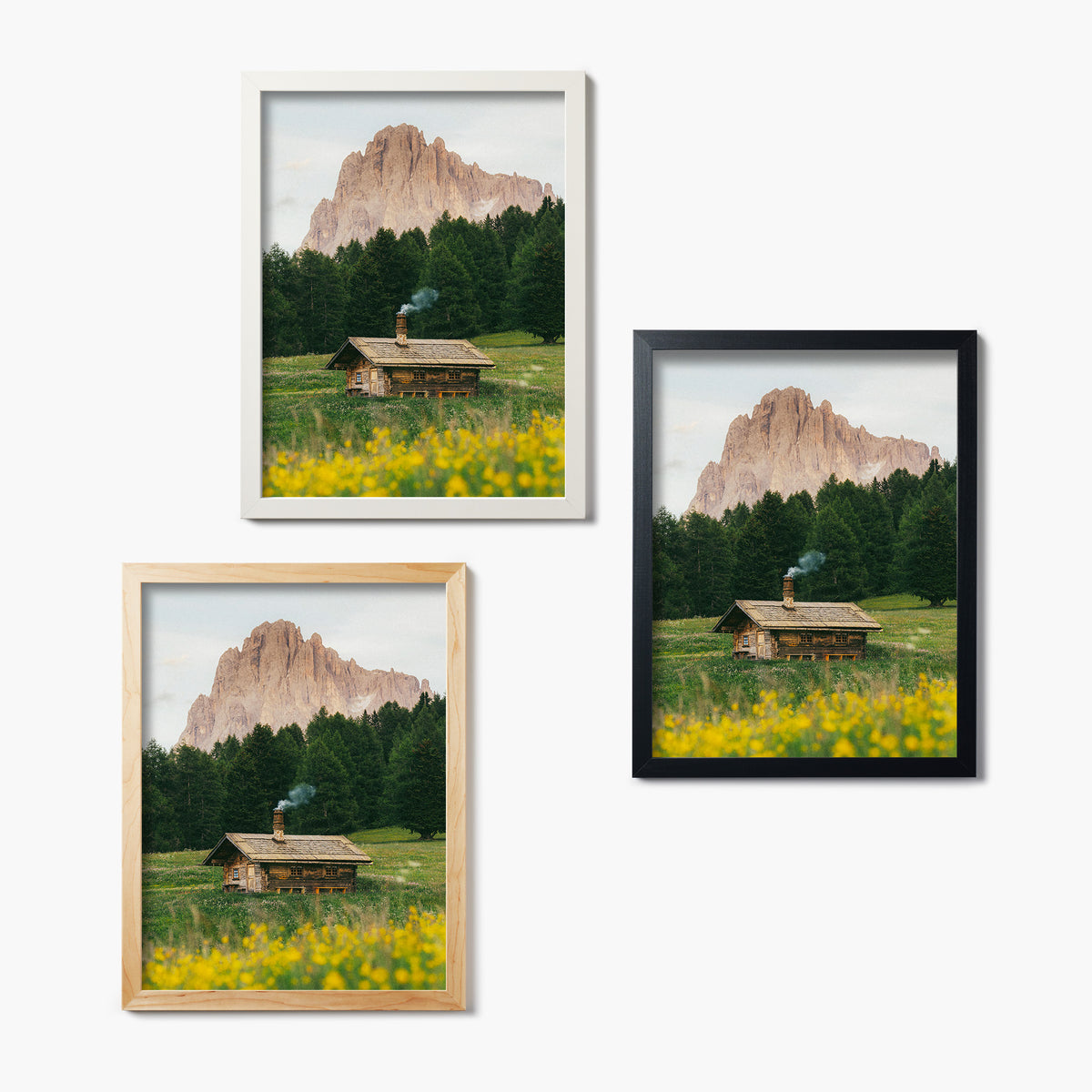 Three framed glass prints of a mountain landscape with a cabin and yellow flowers.