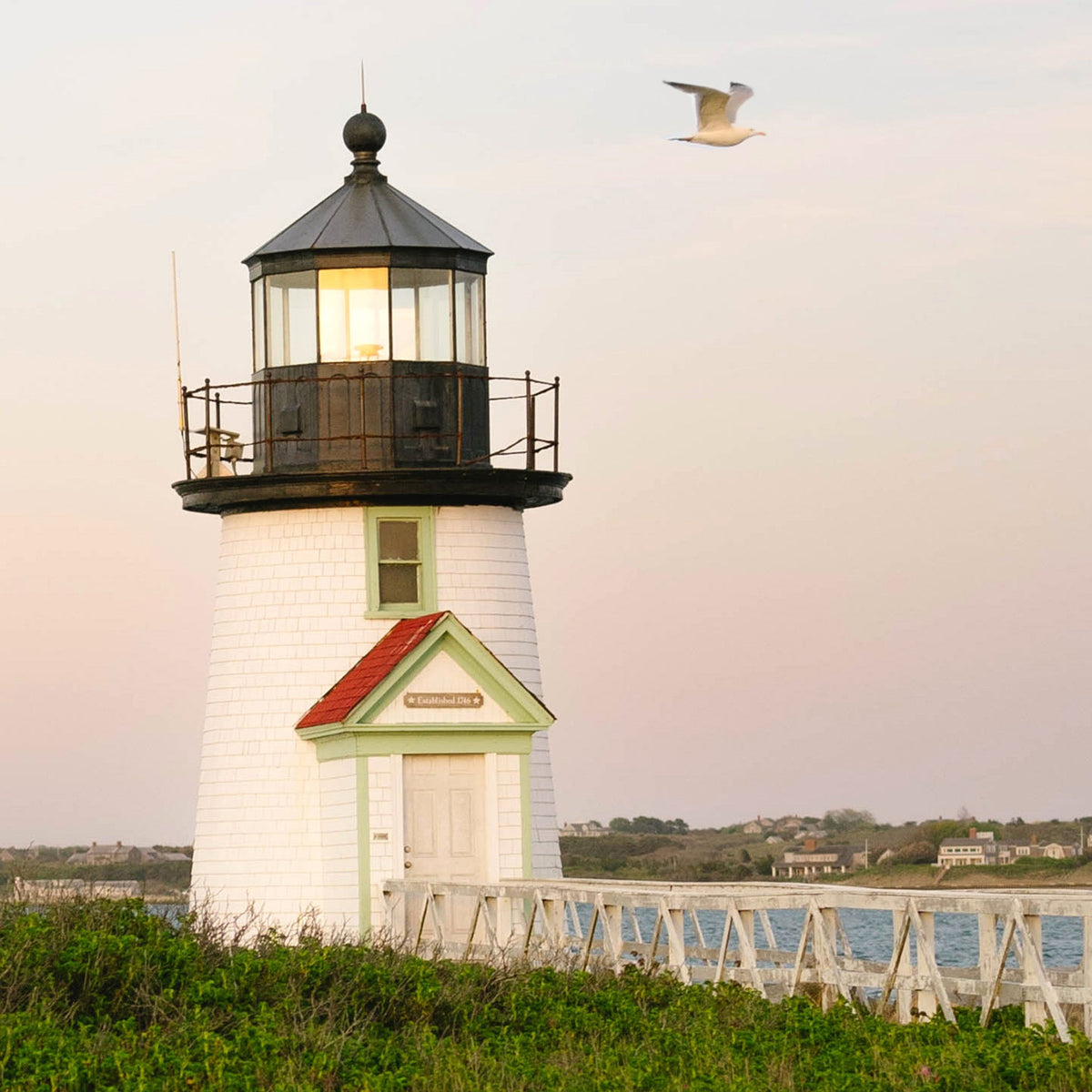 Close up of a lighthouse with a bird flying above it against a pink-hued sky