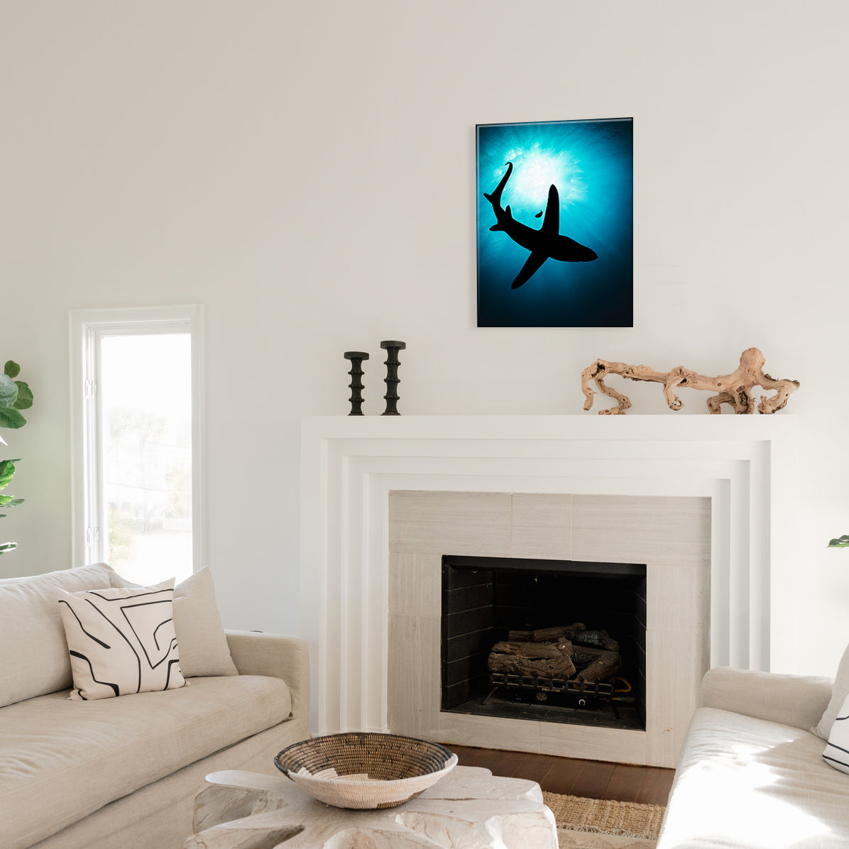A glass print of a shark and solo fish silhouetted against a blue background, hanging above a fireplace in a living room.