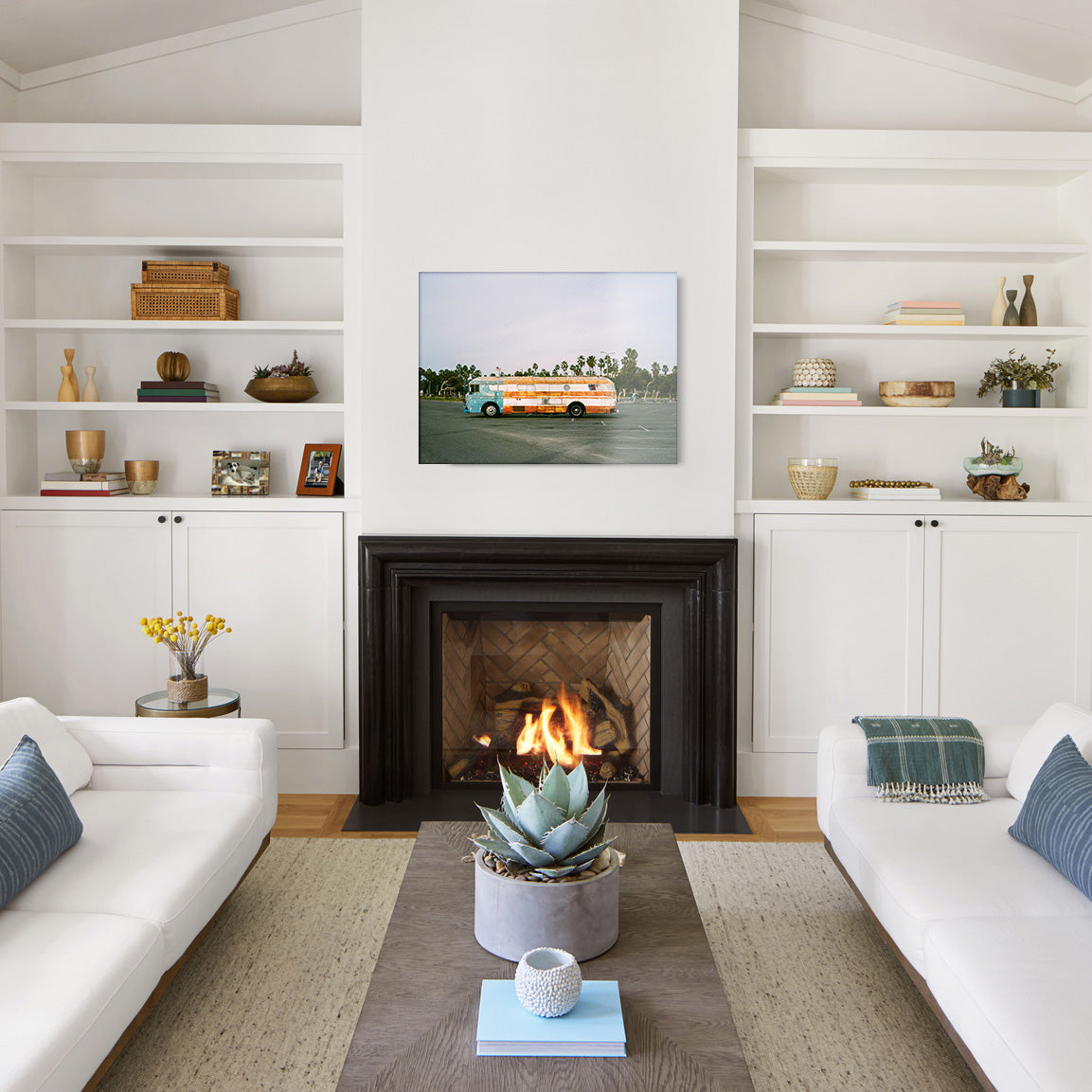 Modern living room with white walls, a fireplace, and a glass print of a vintage Americana decorated bus in a parking lot.