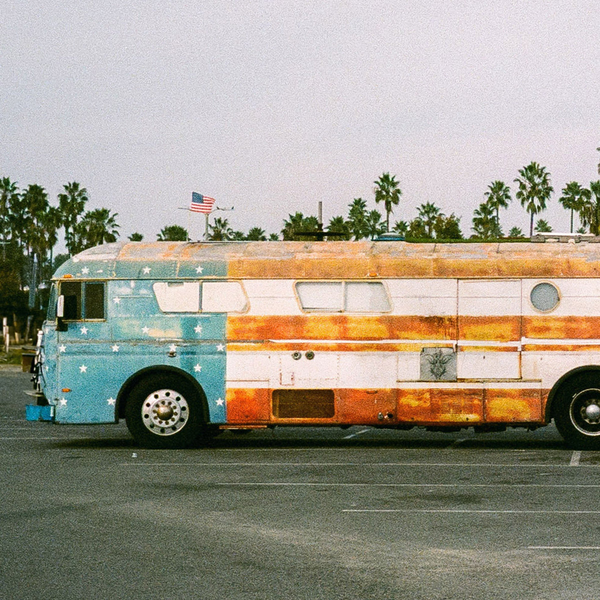 Close-up of a vintage-style bus with a colorful Americana design in a parking lot with palm trees in the background