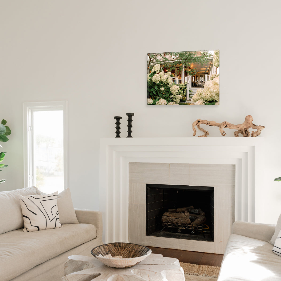 Living room with a fireplace, decorative items, and a glass print of a porch covered in white hydrangeas on the wall.