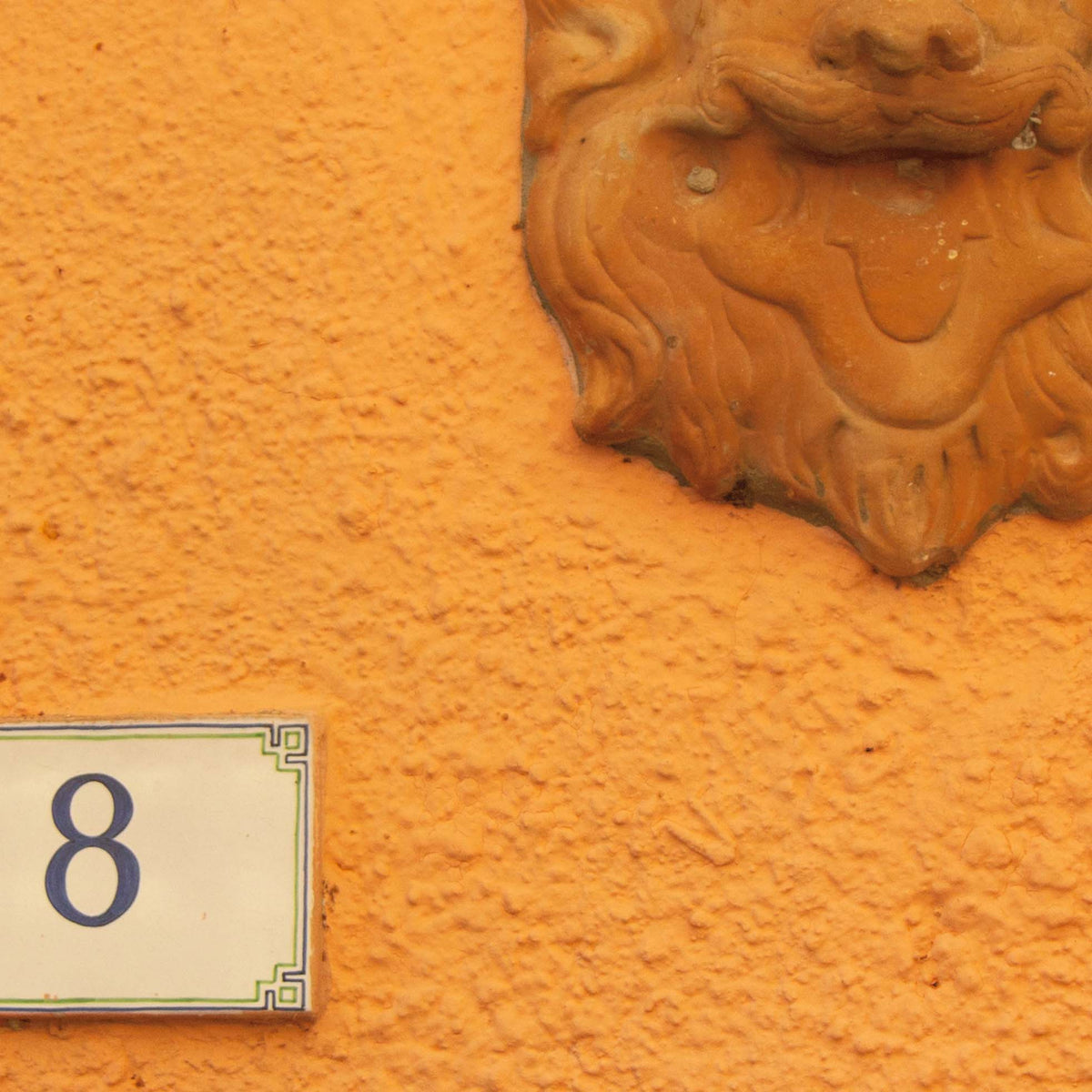 Close-up of decorative lion head on an orange wall with a number 8 plaque.