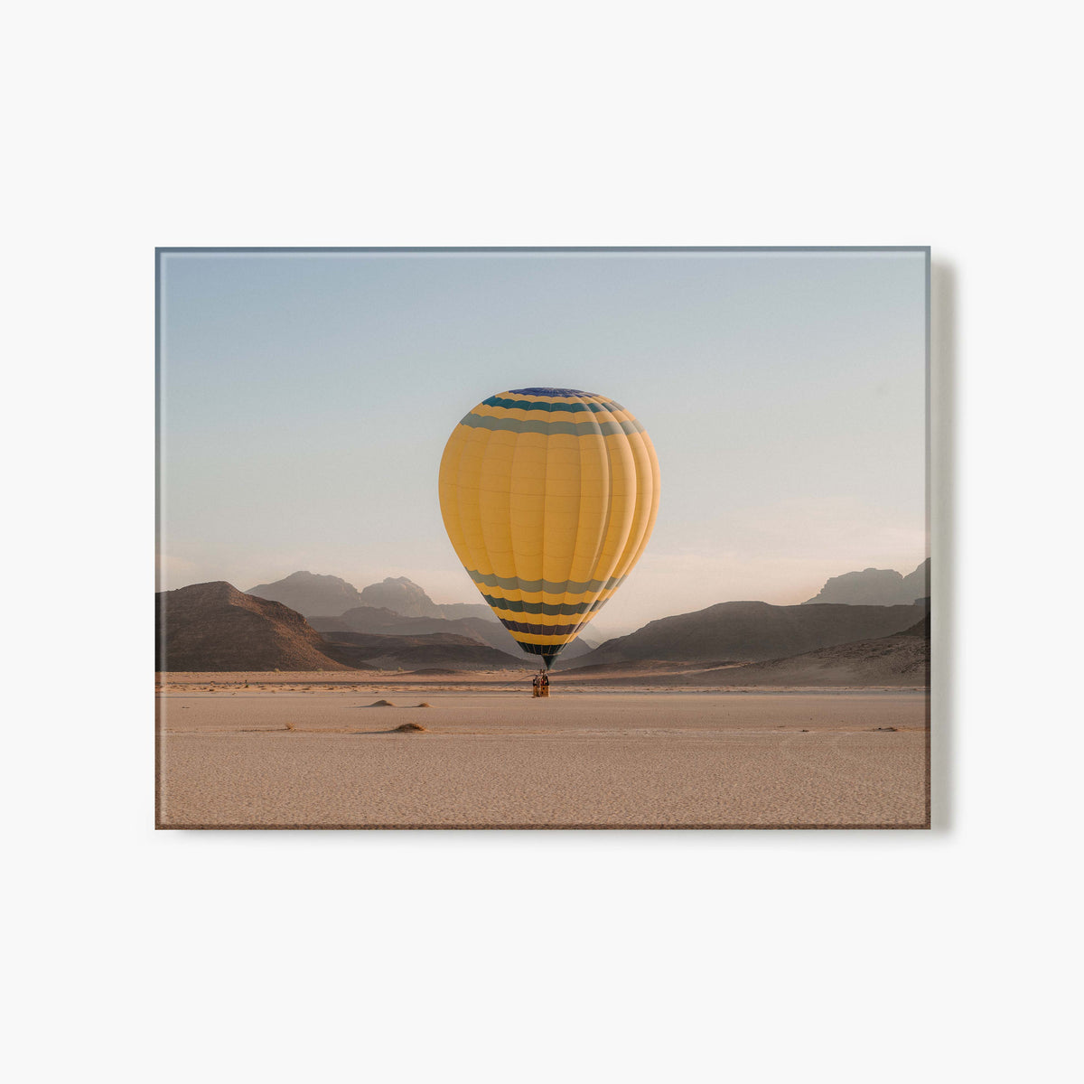 Glass Print of yellow hot air balloon with blue stripes flying over a desert landscape.