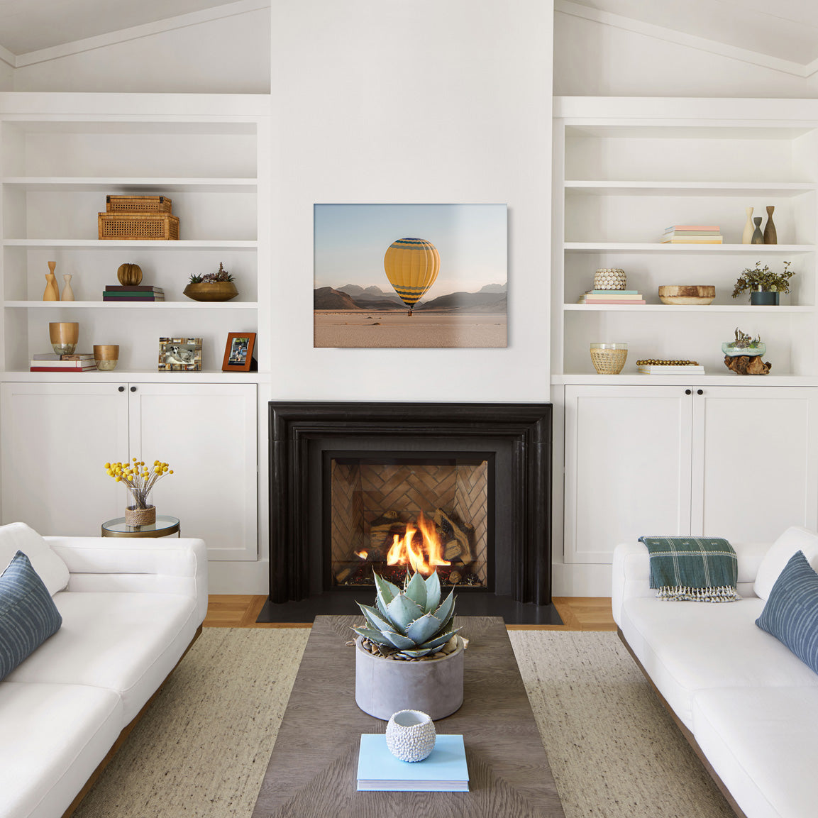 Modern living room with white walls, a fireplace, and a glass print of a yellow hot air balloon in the desert.