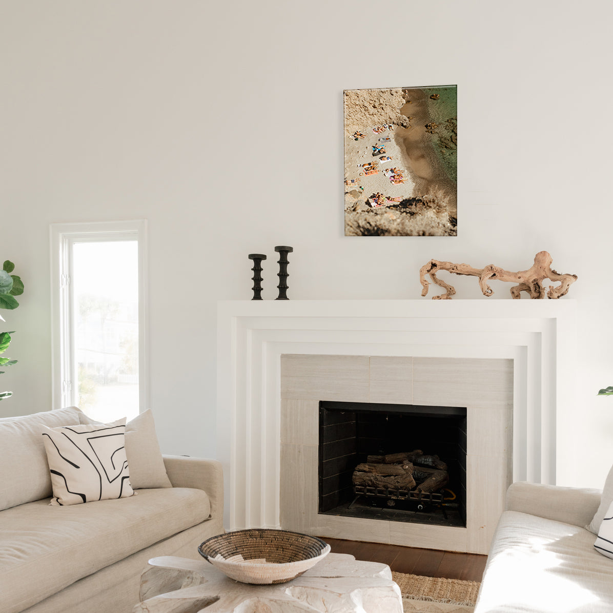 Living room with a fireplace, a glass print of an aerial view of people sunbathing on the coast, and decor items.