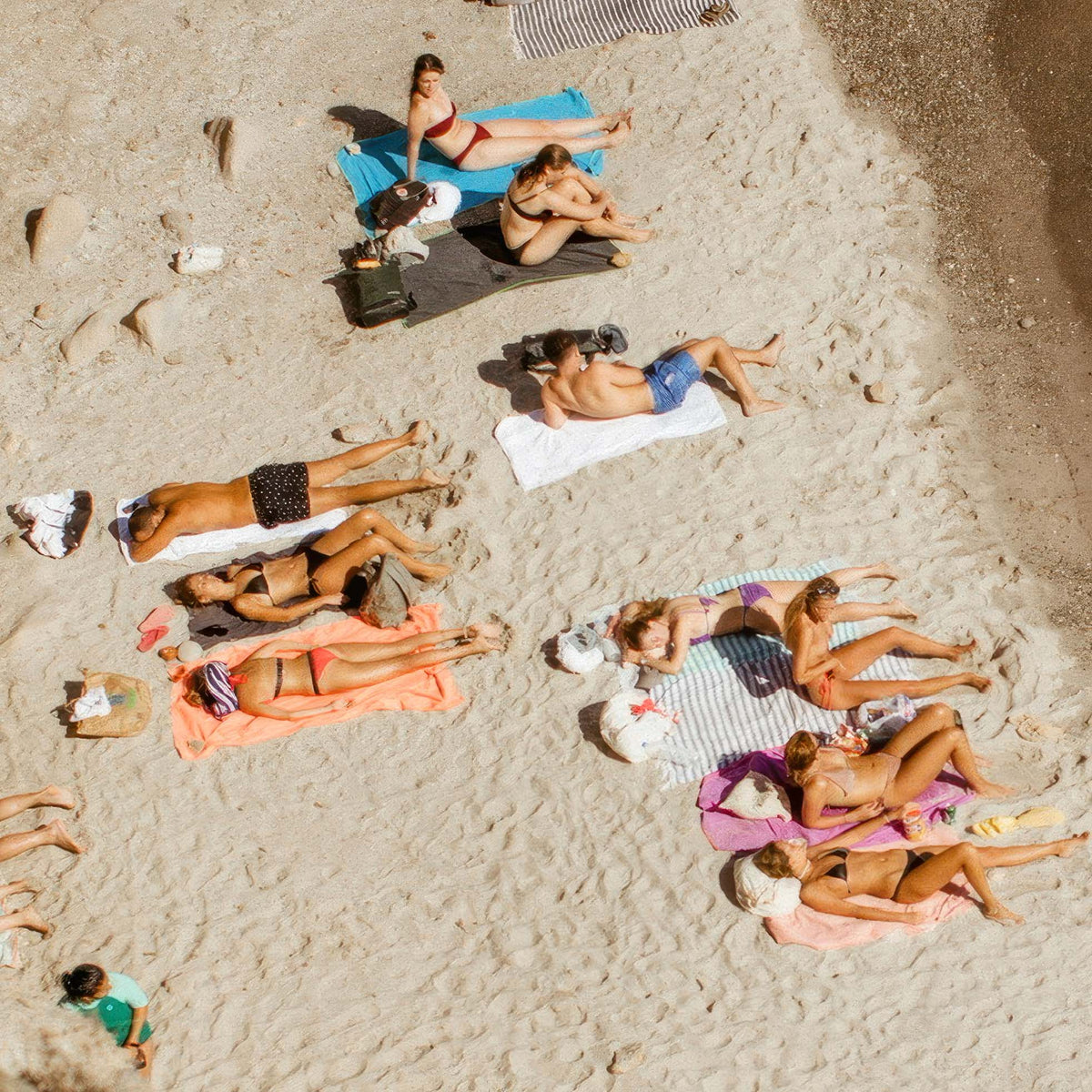Close-up of aerial view of people sunbathing on a sandy beach with towels and blankets.