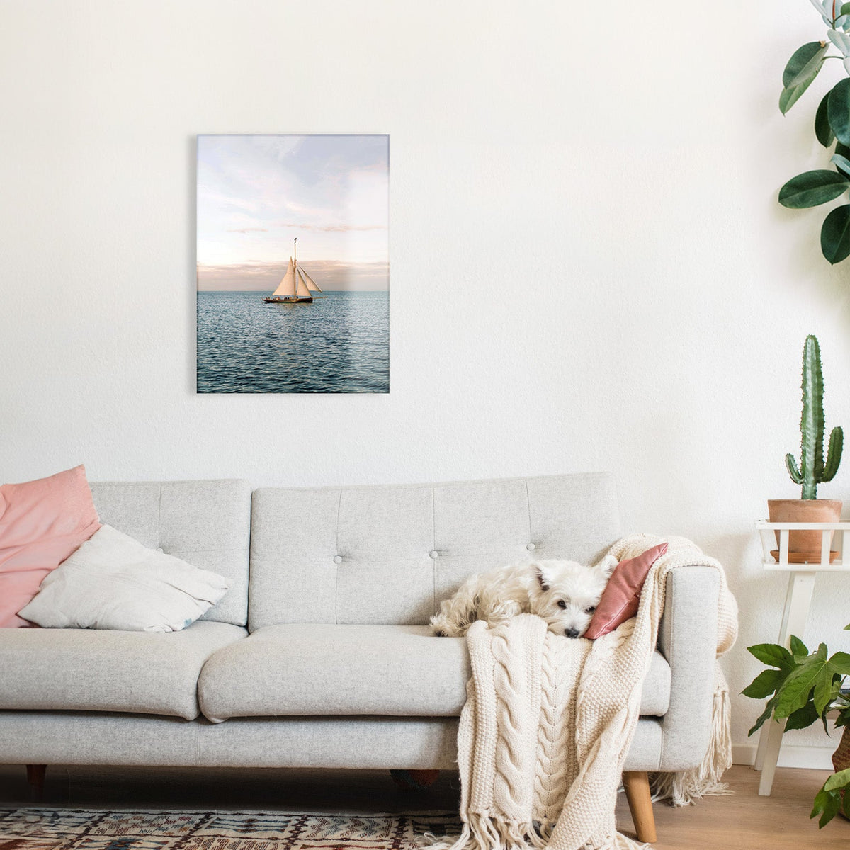 Living room with a gray sofa, pink pillows, and a glass print of a sailboat on the wall.