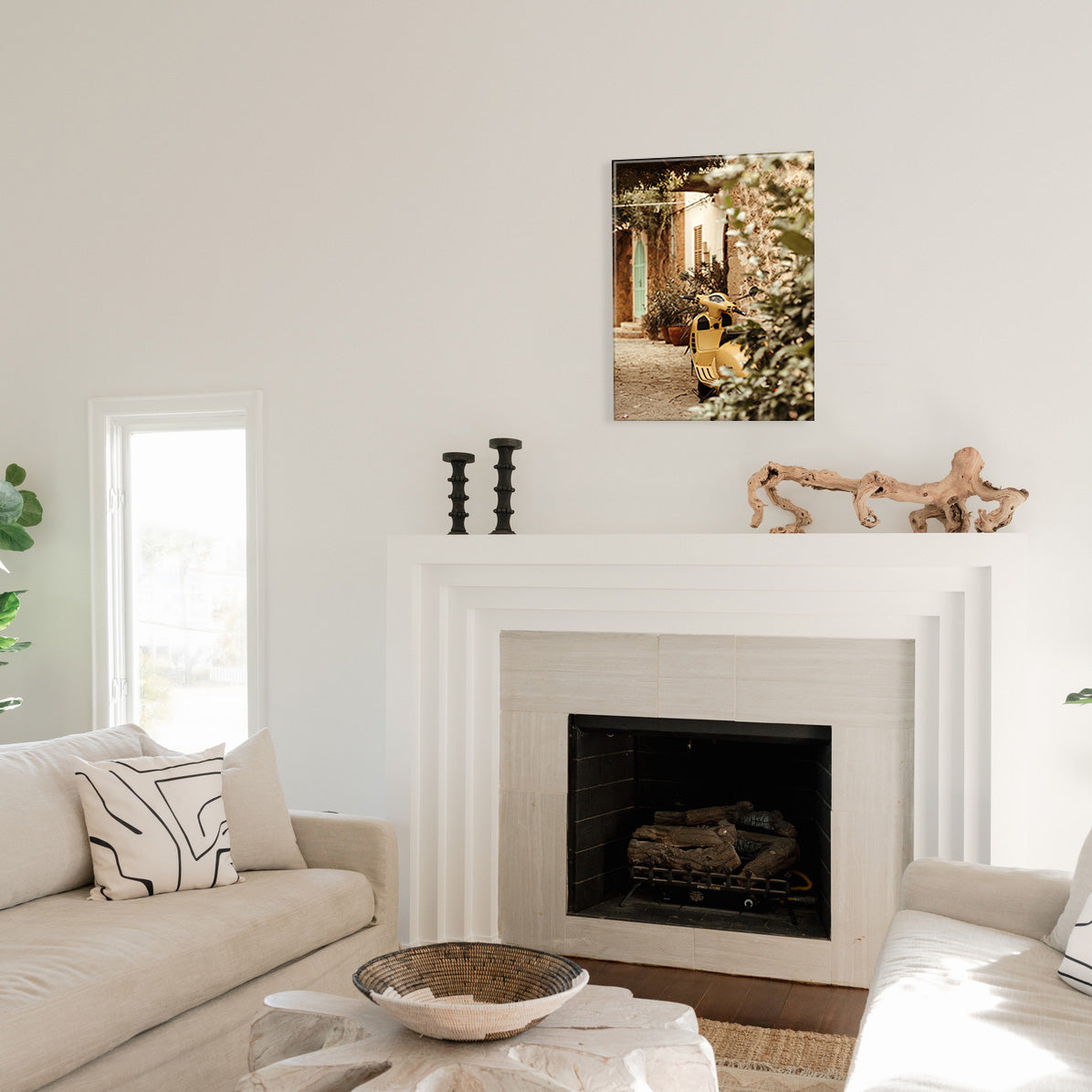 Living room with a fireplace, decorative items, and a glass print of a yellow scooter on a cobblestone street.