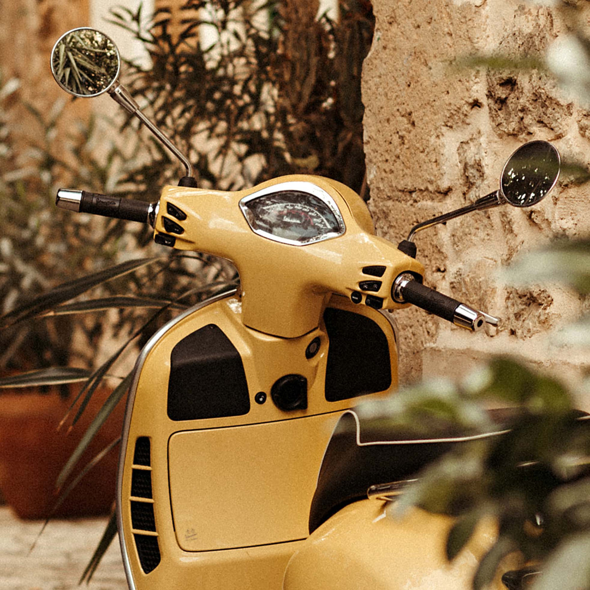 Close-up of vintage yellow scooter with a stone wall and plants in the background