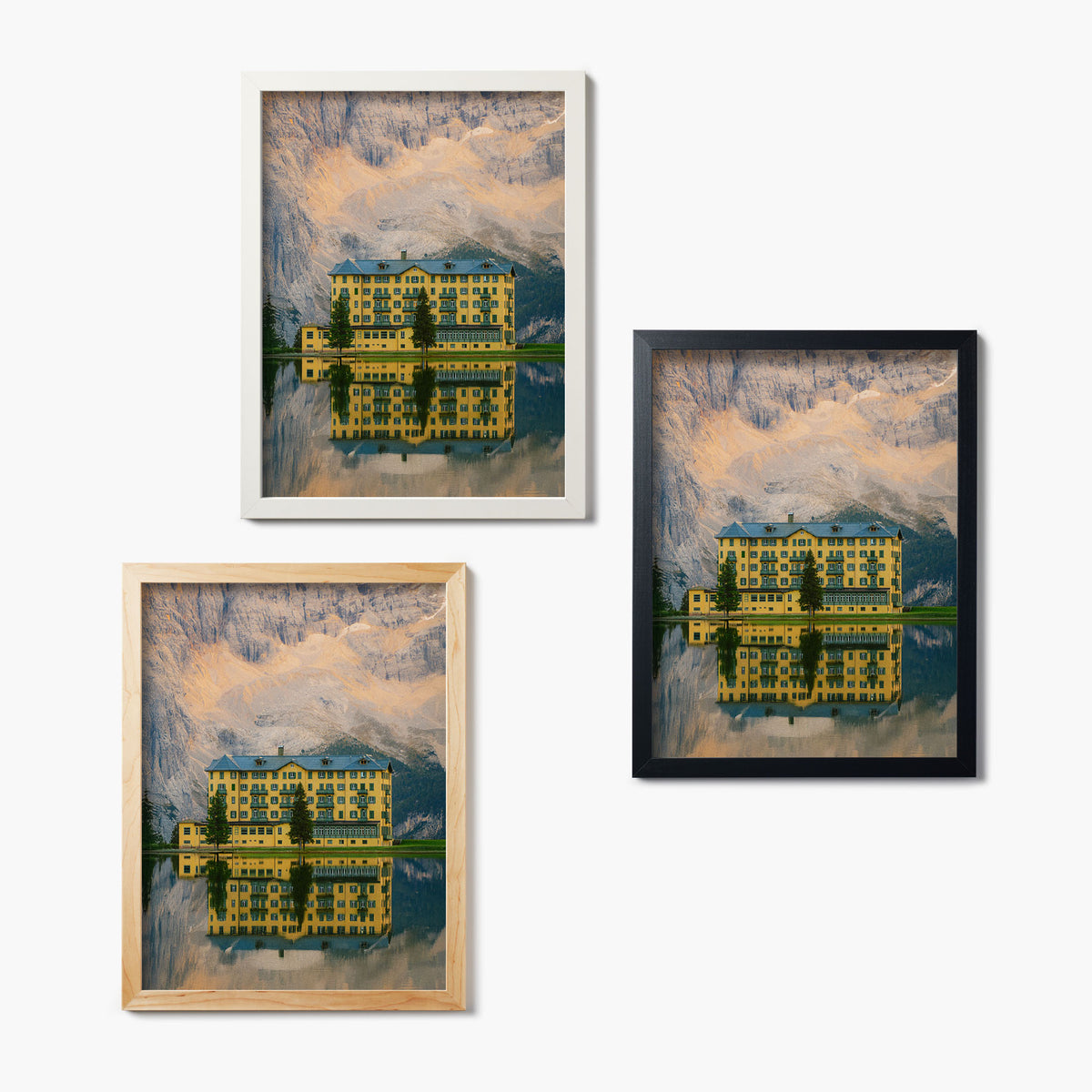 Three framed glass prints of a grand yellow hotel on the edge of a reflective lake with a mountain backdrop.