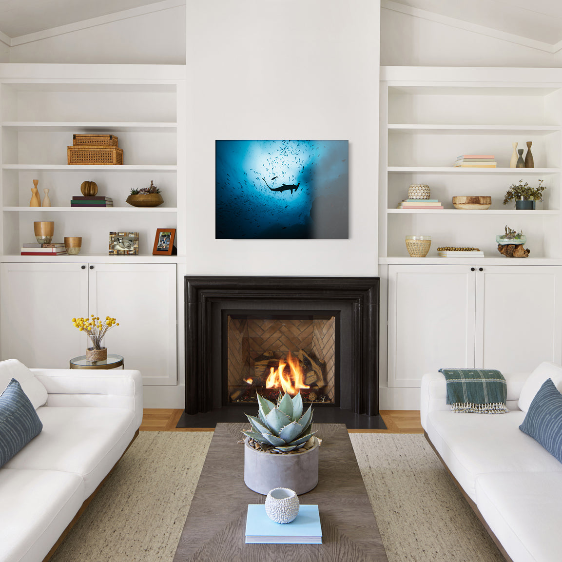 Modern living room with white walls, a fireplace, and decorative shelves—with a large glass print of a hammerhead shark silhouette hanging above the mantel.