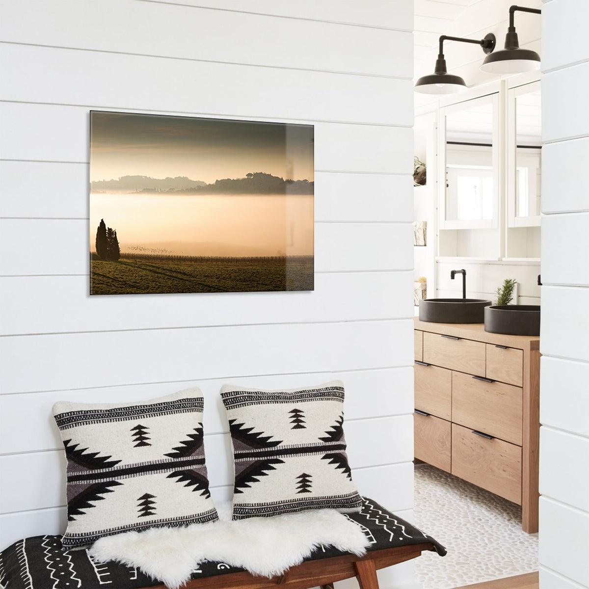 Decorative pillows on a bench with a glass print of a vineyard at sunset above it.